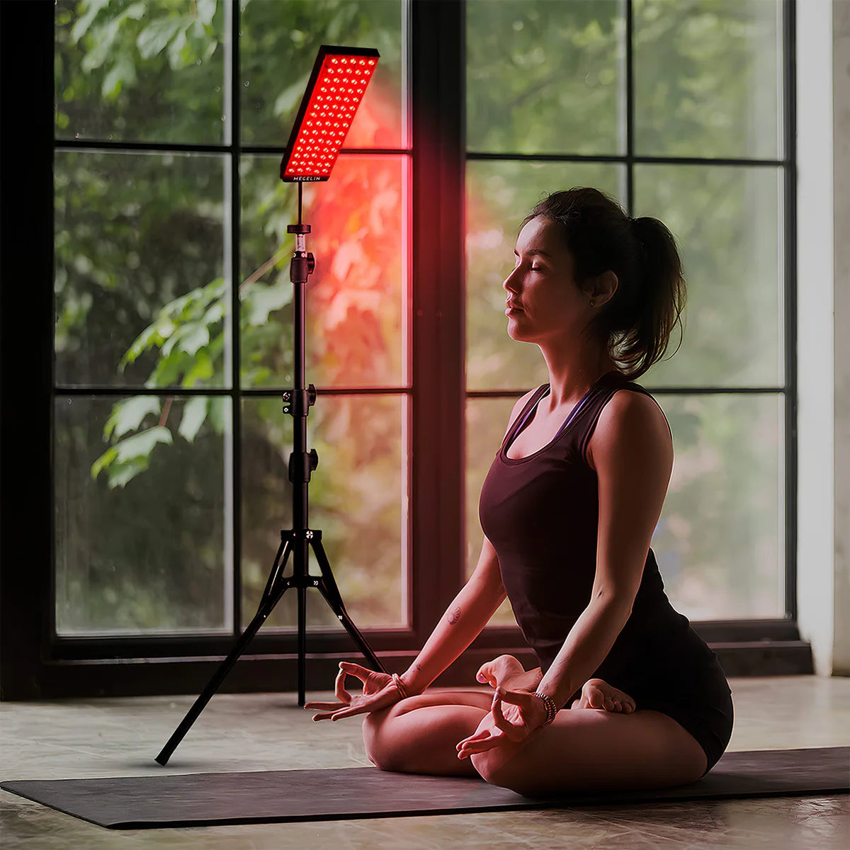 Personne méditant sur un tapis de yoga, baignée dans la lumière apaisante d'un panneau de photothérapie infrarouge.