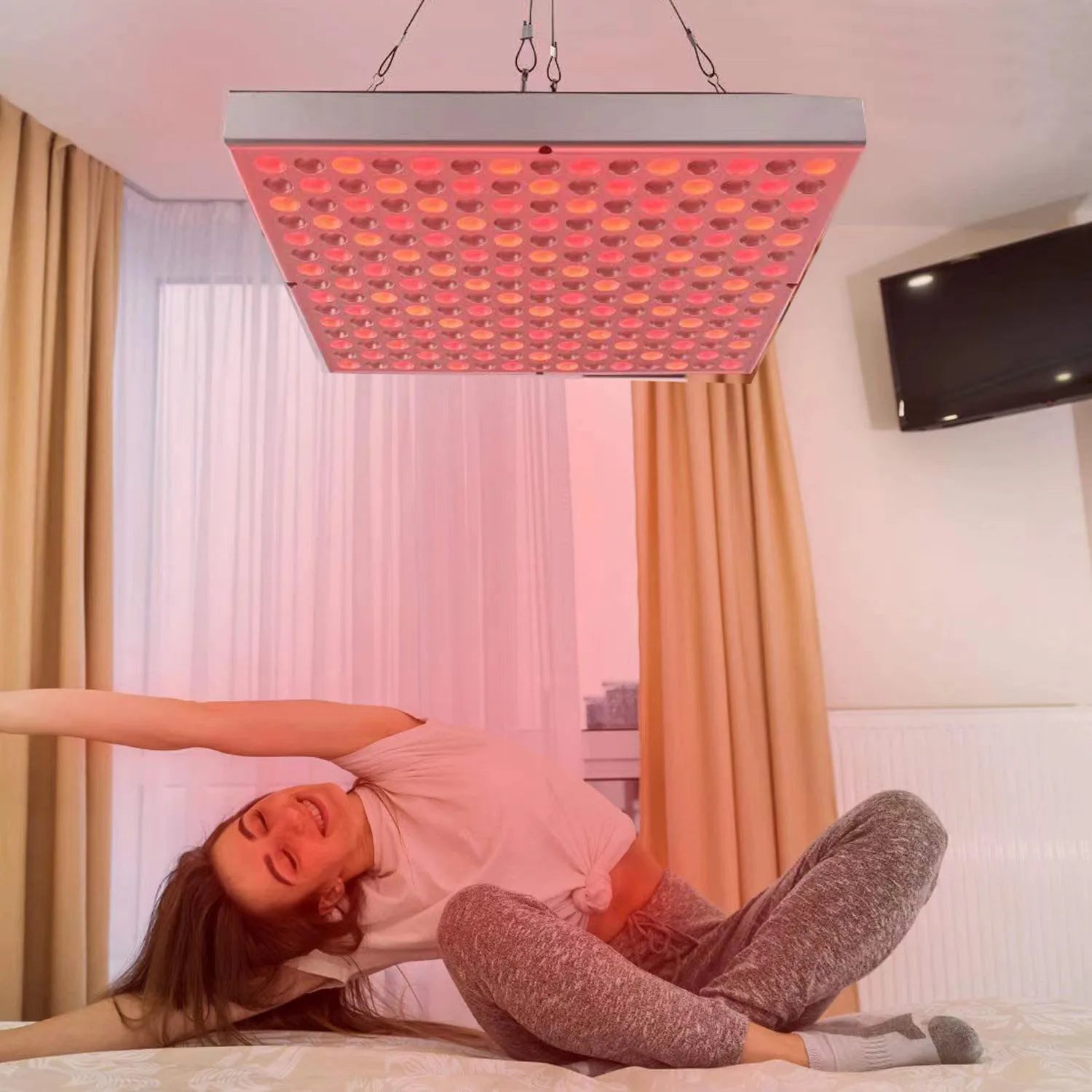 Femme se relaxant sur un lit sous la lumière thérapeutique du panneau de photothérapie DermaLuxe™ suspendu.
