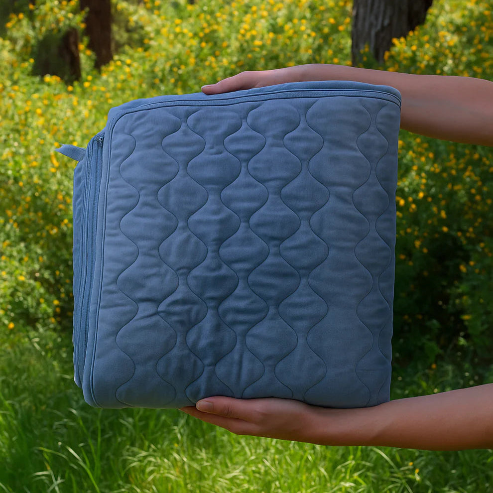 Couverture chauffante 12V ThermoNomad™ pliée, tenue dans les mains pour montrer sa taille compacte idéale pour le voyage