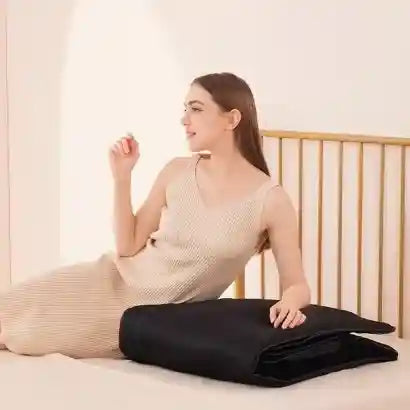Femme assise sur un lit à côté du tapis de massage AeroForm™ entièrement plié, illustrant sa compacité et sa facilité de rangement.